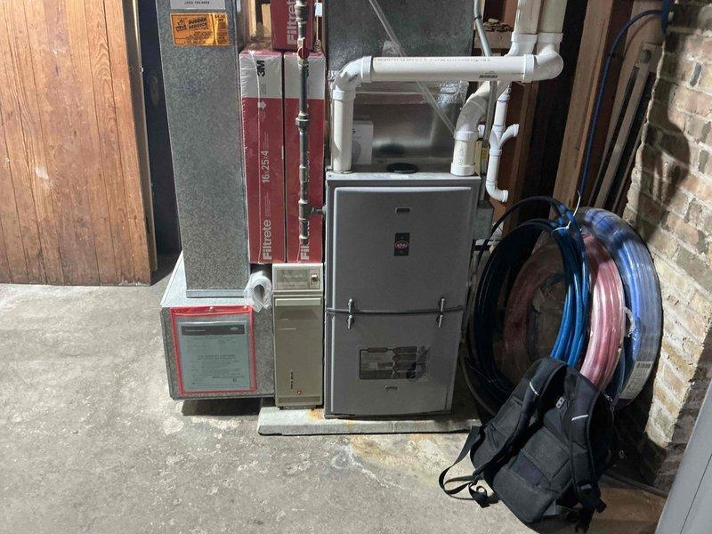 Completed installation of a Carrier air conditioning system with dual outdoor condensers positioned on a snow-covered ground adjacent to the client's vinyl-sided residence. The installation included proper electrical connections and refrigerant line setup. In the basement utility room, installed a new furnace unit with complete PVC ventilation system and organized refrigerant line connections. All components were properly secured and tested for functionality.