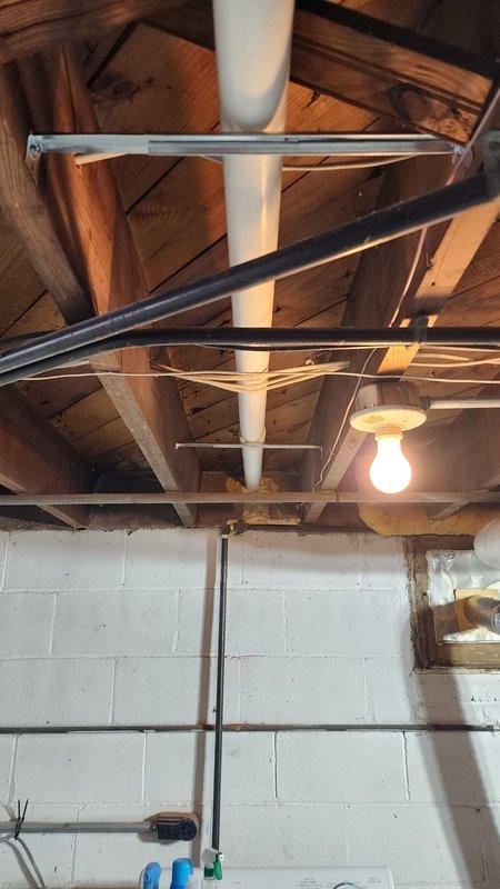 Completed warranty installation of residential HVAC system in basement utility area, including proper mounting of furnace unit with all required copper and PVC piping connections. Installed system features red control valve and multiple brass fittings, with all components securely fastened to ceiling joists and structural framework for optimal performance.