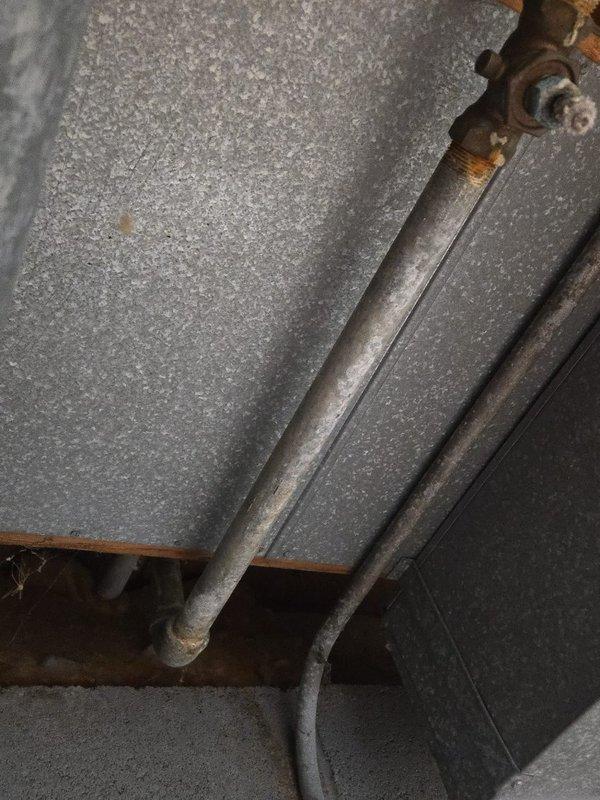 Inspected plumbing system and identified significant corrosion and oxidation on metal pipe fittings, particularly at T-junction/valve assembly and connection points. Documented extensive rust formation on aging pipes in utility area, with deterioration most severe at junction points.