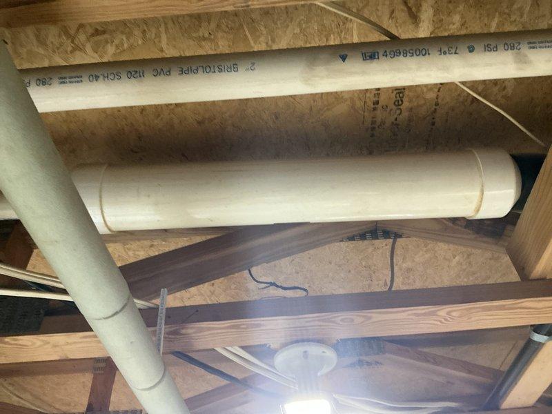 Completed installation of a new residential HVAC system including a beige furnace unit with associated copper lines, electrical connections, and control components in the utility area. System installation included proper connection to existing PVC drainage/ventilation pipes mounted along wooden joists, with all required plumbing and electrical work completed to ensure optimal system function.