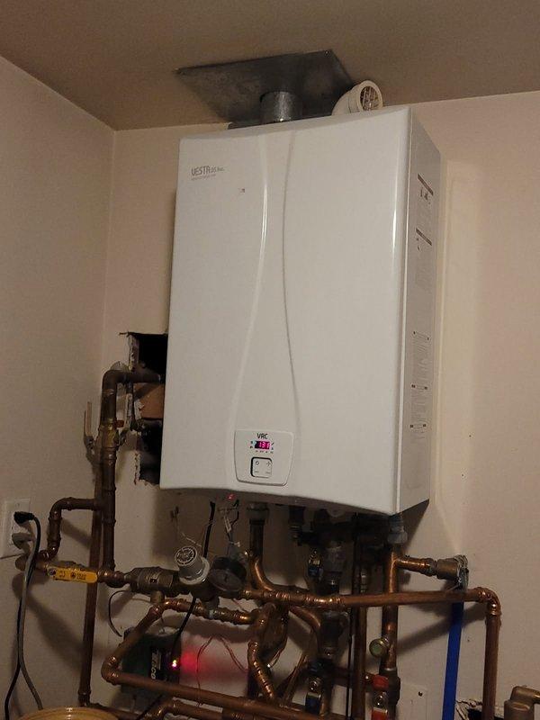 Performed diagnostic inspection on USTR Plus wall-mounted boiler system. Accessed internal components to evaluate operational status, noting temperature reading of 83.6°F on control panel. Inspected copper supply lines, valves, and circulation pump for proper function and confirmed adequate ventilation through ceiling duct connection.