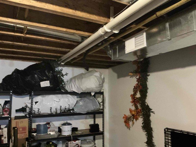 Performed comprehensive inspection and documentation of existing HVAC system in residential basement. System includes furnace unit with sheet metal housing connected to vertical PVC ventilation pipes, side-mounted humidifier, and rectangular metal ductwork running along ceiling joists. Photos captured both the main mechanical room setup and adjacent storage area with exposed infrastructure for complete system evaluation prior to replacement estimate.