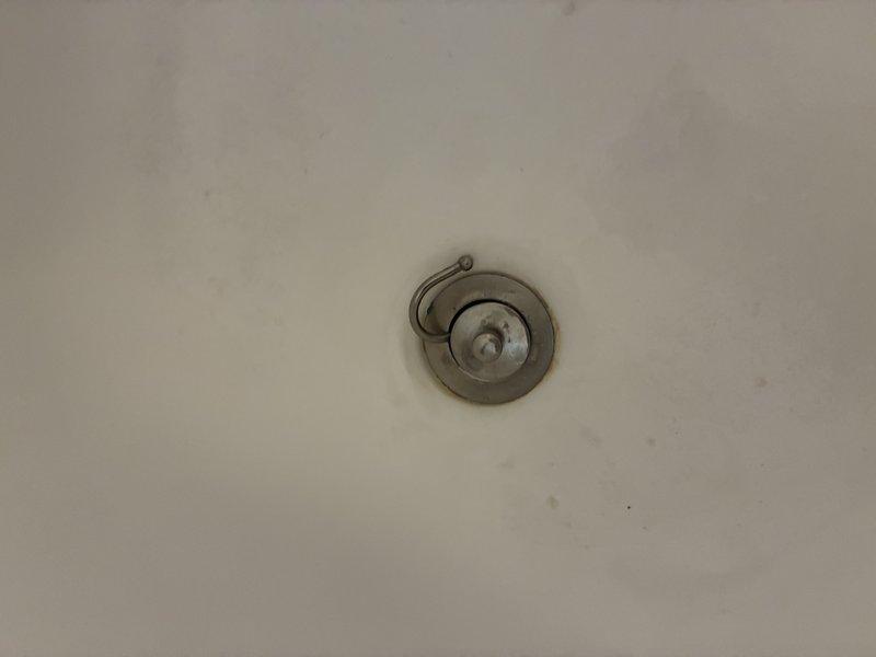 Replaced deteriorated chrome drain assembly in bathroom fixture with new pop-up drain mechanism. Removed old fixture showing signs of water damage and tarnishing, then installed and sealed new drain assembly. Verified proper operation of stopper mechanism and confirmed no leaks present.