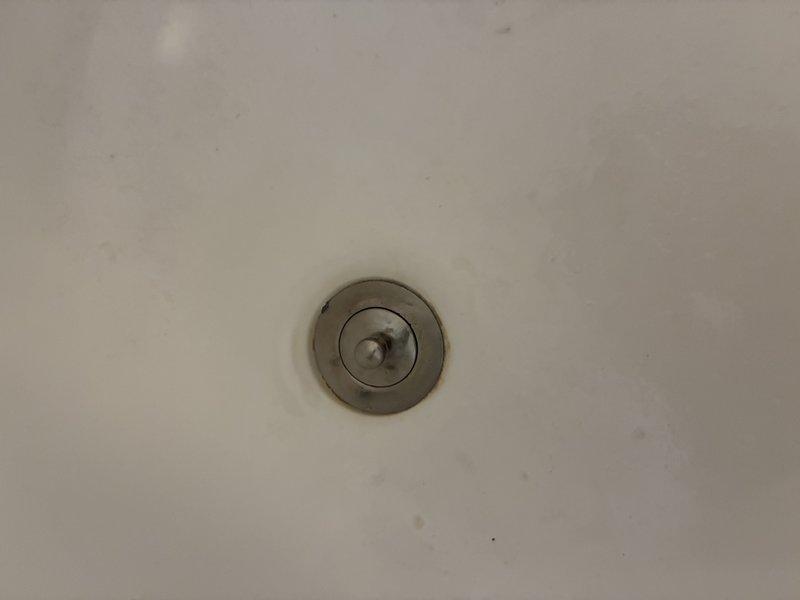 Replaced deteriorated chrome drain assembly in bathroom fixture with new pop-up drain mechanism. Removed old fixture showing signs of water damage and tarnishing, then installed and sealed new drain assembly. Verified proper operation of stopper mechanism and confirmed no leaks present.