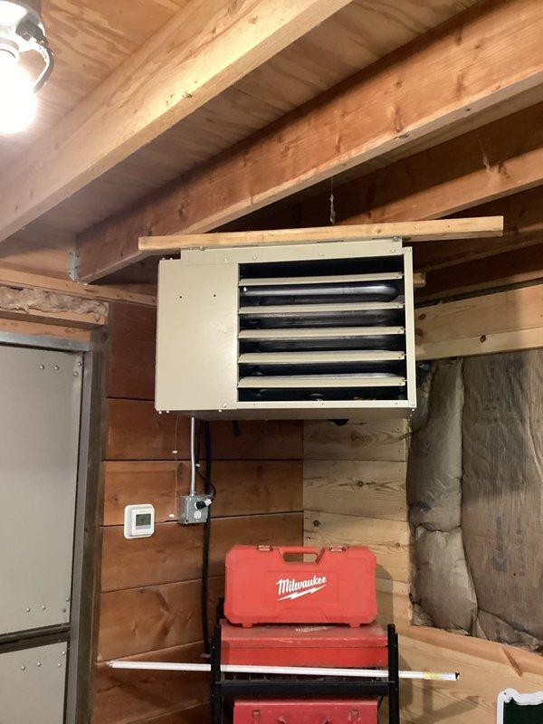 Inspected and serviced wall-mounted HVAC unit in workshop area, verifying proper connection of ductwork to system. Confirmed all seams and joints in metal ductwork were secure and correctly installed through exposed joists, with particular attention to the curved section and connection points to smaller conduits.