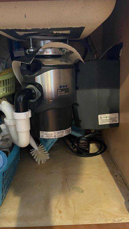 Conducted inspection of kitchen sink plumbing system, focusing on the existing garbage disposal unit and associated connections. Evaluated the stainless steel kitchen faucet with high-arched neck, secondary dispenser, and the PVC drain assembly under the sink. Assessment revealed operational garbage disposal with proper electrical and plumbing connections, requiring no immediate replacement.