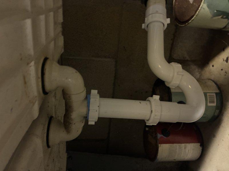 Inspected existing drainage system beneath sink, which showed signs of aging and minor discoloration on PVC P-trap assembly and connecting pipes. Evaluated condition of multiple connection points, threaded coupling joints, and elbow configurations in the confined utility space, noting proper alignment to wall drain despite age-related wear.