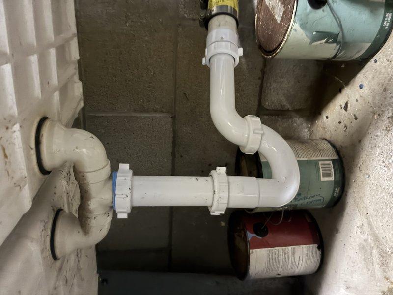 Inspected existing drainage system beneath sink, which showed signs of aging and minor discoloration on PVC P-trap assembly and connecting pipes. Evaluated condition of multiple connection points, threaded coupling joints, and elbow configurations in the confined utility space, noting proper alignment to wall drain despite age-related wear.