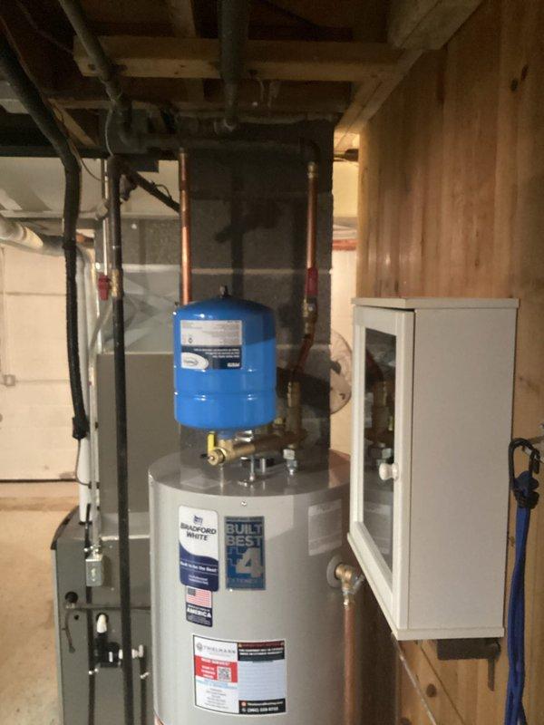 Installed a new hot water heater system in residential basement with appropriate copper pipe connections and valves. System includes a blue expansion tank mounted above the water heater and all necessary safety valves. Completed installation with proper connections to existing plumbing infrastructure.