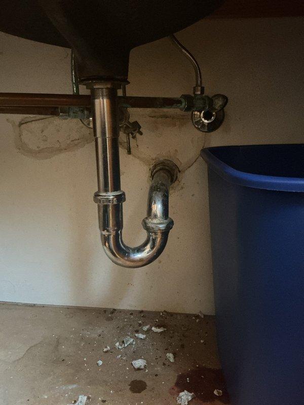 Conducted plumbing assessment of residential drainage system, identifying water damage around sink P-trap connections and inspecting basement PVC drainage piping. Documented existing conditions including pipe corrosion at connection points and evaluated the integrity of mounting hardware securing vertical drain lines to structural elements.