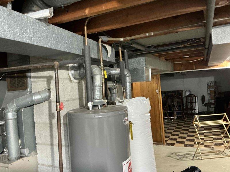 Conducted site inspection of dual outdoor condensing units requiring replacement, documenting their current installation on concrete pads adjacent to gas meters and drainage infrastructure. Interior assessment of mechanical room revealed integration with existing water heater system and associated plumbing, with particular attention to connection points requiring modification during HVAC system replacement.