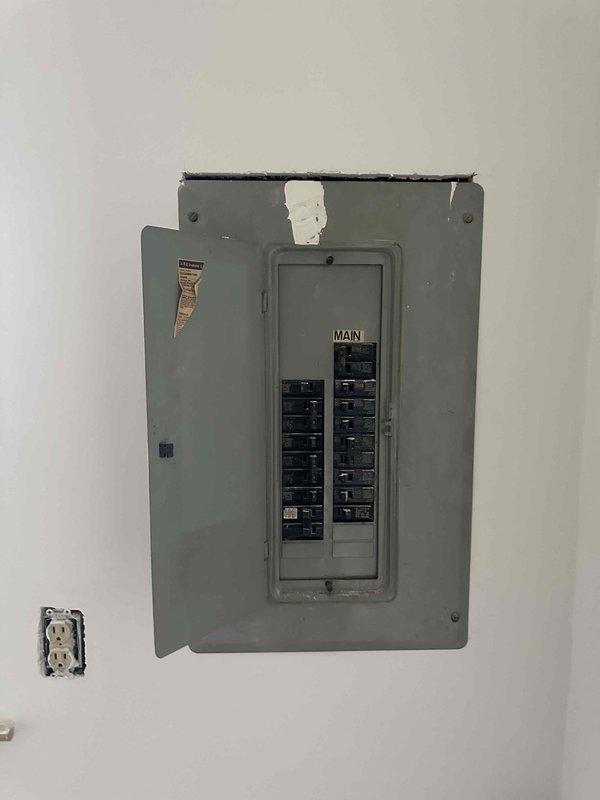 Conducted evaluation of aging two-tone furnace/air handler system installed in confined utility space, showing signs of wear and possible moisture issues. Inspected electrical panel with visible damage at top edge and exposed outlet without faceplate. Recommended complete system replacement due to equipment age, installation constraints, and electrical safety concerns.