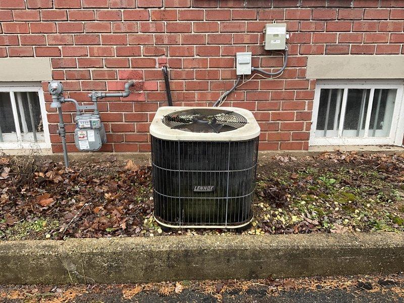 Performed visual inspection of aged Lennox outdoor condensing unit (Model HP24-251-1P, Serial #51928188B) showing significant weathering, dirt accumulation, and biological growth on exterior surfaces. Unit positioned against brick wall adjacent to gas meter with visible utility connections. Assessment indicates system has reached end of serviceable life and full replacement is recommended to restore optimal cooling efficiency and reliability.
