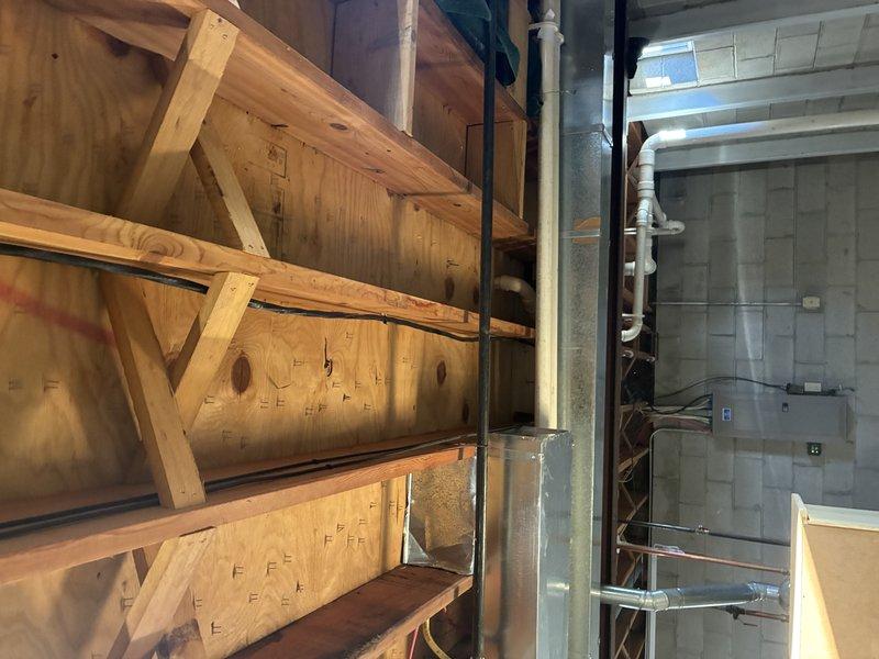 Conducted a thorough assessment of existing plumbing infrastructure at the junction between wooden framing and concrete block foundation wall. Evaluated PVC vertical piping runs along the concrete block wall in the utility area, documenting condition and placement relative to electrical panel and structural elements. Photos were taken to document the current installation for detailed estimate preparation.