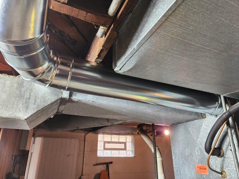 Successfully installed new galvanized sheet metal ductwork in basement utility area, including horizontal main trunk line with vertical branch connection. System was properly secured to wooden joists and framing members, with all connections sealed and fastened according to specifications.