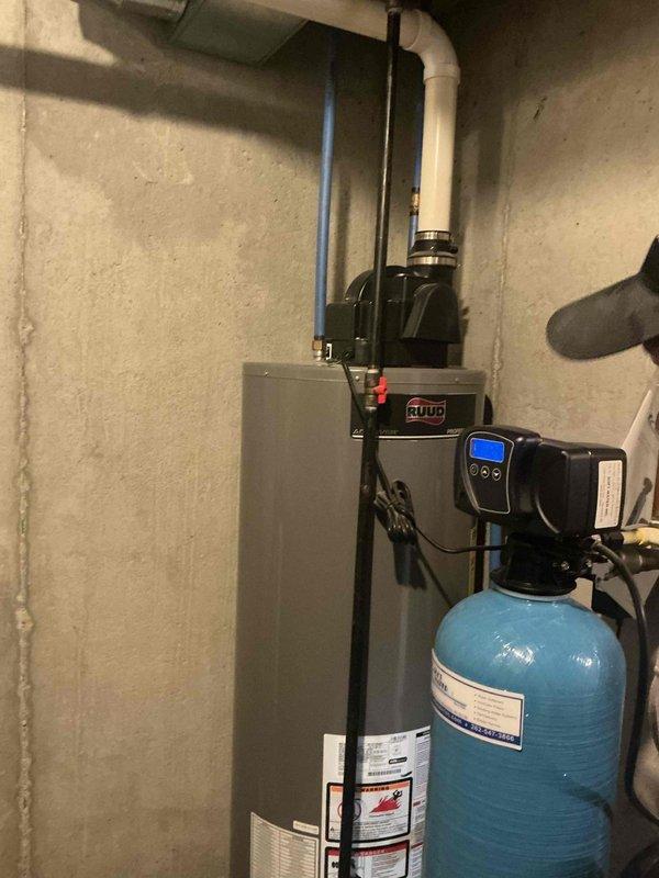 Inspected Ruud tanked water heater system and adjacent water filtration equipment in basement utility area. Performed routine maintenance on water heater, checking connections and verifying proper operation of temperature and pressure relief valve. Confirmed water treatment system with digital control head was functioning correctly and properly integrated with the water heater setup.