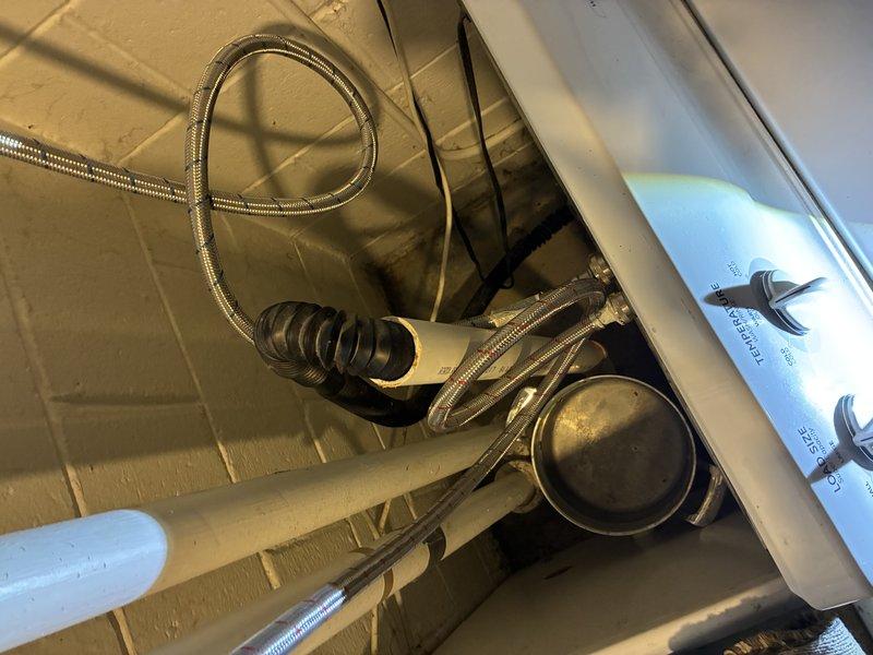 Performed inspection of under-sink plumbing assembly, including PVC pipes, braided supply lines, and accordion-style drain pipe. Examined valve installation with visible wall penetration issues in utility area. Documented condition of plumbing components and identified potential maintenance needs for future service.