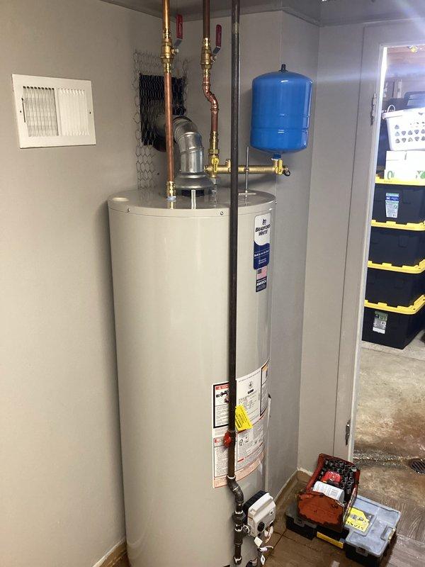 Completed installation of a new residential water heater system with proper connections to existing plumbing. Installed blue expansion tank with copper pipes and brass valves on top of the unit, and ensured pressure relief valve was correctly positioned. System was tested for proper operation and all connections were verified leak-free before completing the job.