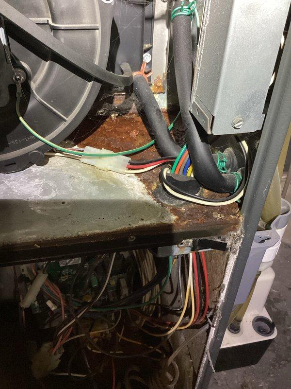 Performed diagnostic assessment on aging furnace system with significant oxidation and corrosion on internal components. Inspected electrical connections and wiring harnesses, noting multiple colored wires (green, red, orange, white) requiring attention. Serviced blower motor assembly and completed necessary repairs to address deterioration of metal chassis and mounting brackets.