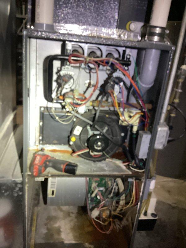 Performed diagnostic assessment on aging furnace system with significant oxidation and corrosion on internal components. Inspected electrical connections and wiring harnesses, noting multiple colored wires (green, red, orange, white) requiring attention. Serviced blower motor assembly and completed necessary repairs to address deterioration of metal chassis and mounting brackets.