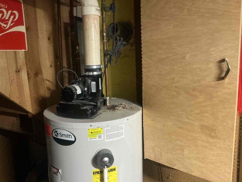 Conducted inspection of existing A.O. Smith electric water heater installation in utility area. Unit appears to have proper connections with PVC piping and circulation pump mounted on top. Noted minor dust accumulation on tank surface. Evaluated current installation configuration against wooden paneling for replacement estimate.