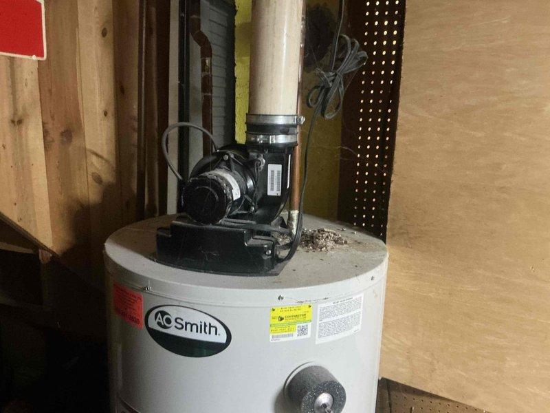 Conducted inspection of existing A.O. Smith electric water heater installation in utility area. Unit appears to have proper connections with PVC piping and circulation pump mounted on top. Noted minor dust accumulation on tank surface. Evaluated current installation configuration against wooden paneling for replacement estimate.