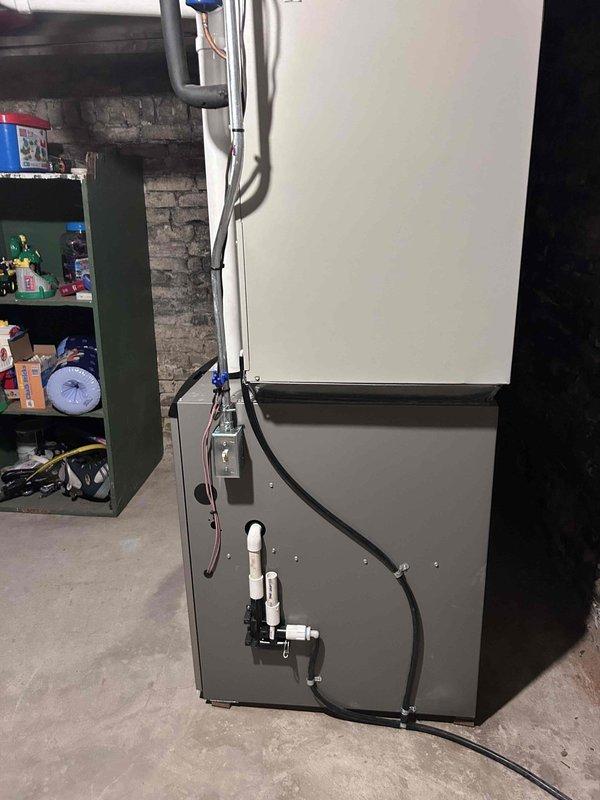 Successfully completed installation of a high-efficiency furnace system in basement utility area, including proper connection of PVC condensate drainage and all necessary electrical components. Unit was securely mounted against concrete block wall with proper clearances maintained, and all connections were tested to verify optimal system performance.