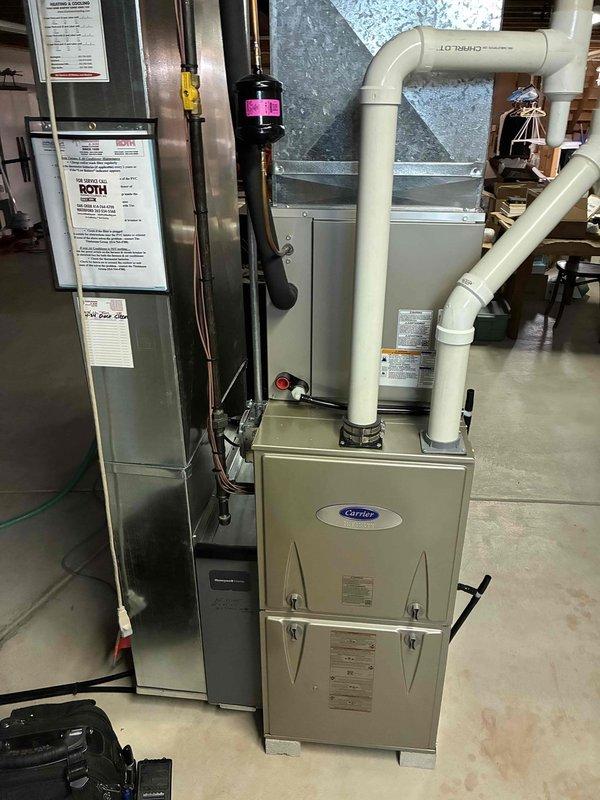 Inspected and serviced Carrier furnace system located in utility area. Verified proper installation of PVC ventilation components, refrigerant lines with filter drier, and all electrical connections. Confirmed Honeywell ProSeries thermostat functioning correctly with heat mode operational and displaying proper temperature (68°F).