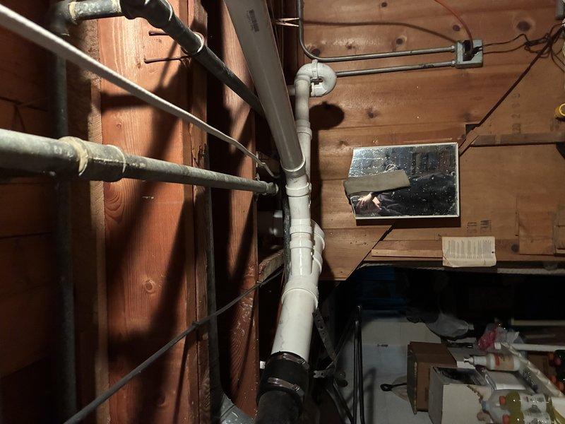 Completed inspection and installation of PVC drainage system for toilet/urinal connection. Installed vertical and horizontal PVC drain pipes through wooden framing, securing with appropriate brackets and straps. Verified proper alignment and pitch of drainage components within the unfinished utility area.