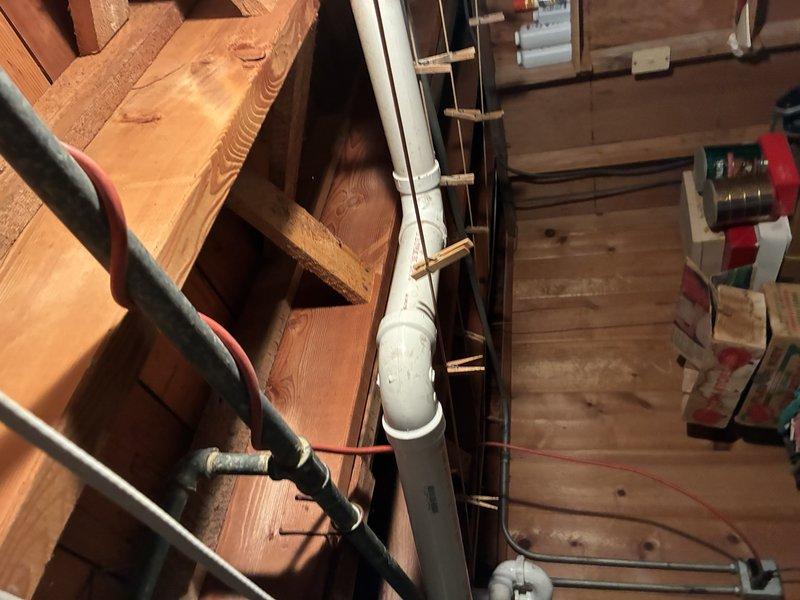 Completed inspection and installation of PVC drainage system for toilet/urinal connection. Installed vertical and horizontal PVC drain pipes through wooden framing, securing with appropriate brackets and straps. Verified proper alignment and pitch of drainage components within the unfinished utility area.