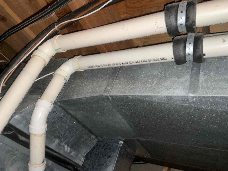 Completed inspection of existing HVAC ducting system in unfinished space, documenting the current PVC ventilation configuration secured to wooden joists with metal clamps. Identified and photographed the electrical breaker panel with the A/C circuit clearly marked to ensure proper connection for the proposed replacement unit.