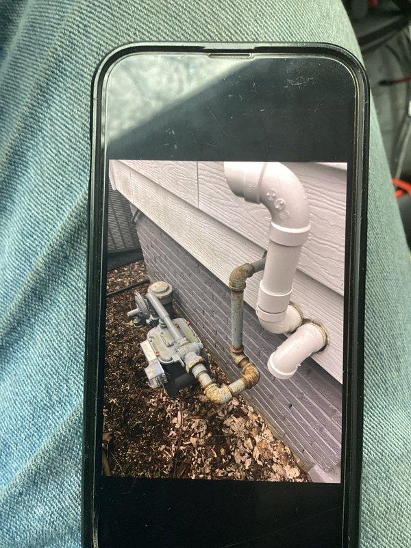 Performed follow-up inspection of exterior plumbing connections where white PVC drainage system meets building's gas service line. Documented significant corrosion and oxidation on metal gas pipes and regulator assembly, with particular deterioration at connection points. Recommended replacement of affected metal components to prevent potential gas leaks while noting the PVC drainage system remains in good working condition.