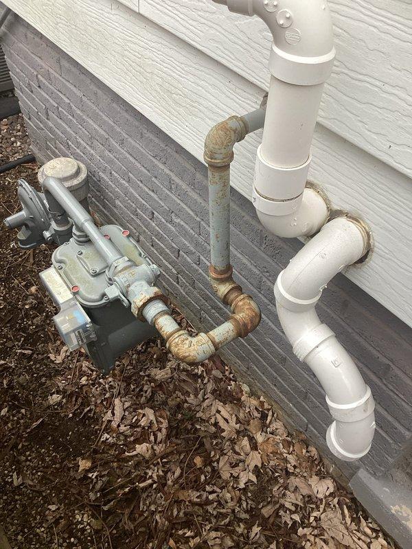 Performed follow-up inspection of exterior plumbing connections where white PVC drainage system meets building's gas service line. Documented significant corrosion and oxidation on metal gas pipes and regulator assembly, with particular deterioration at connection points. Recommended replacement of affected metal components to prevent potential gas leaks while noting the PVC drainage system remains in good working condition.