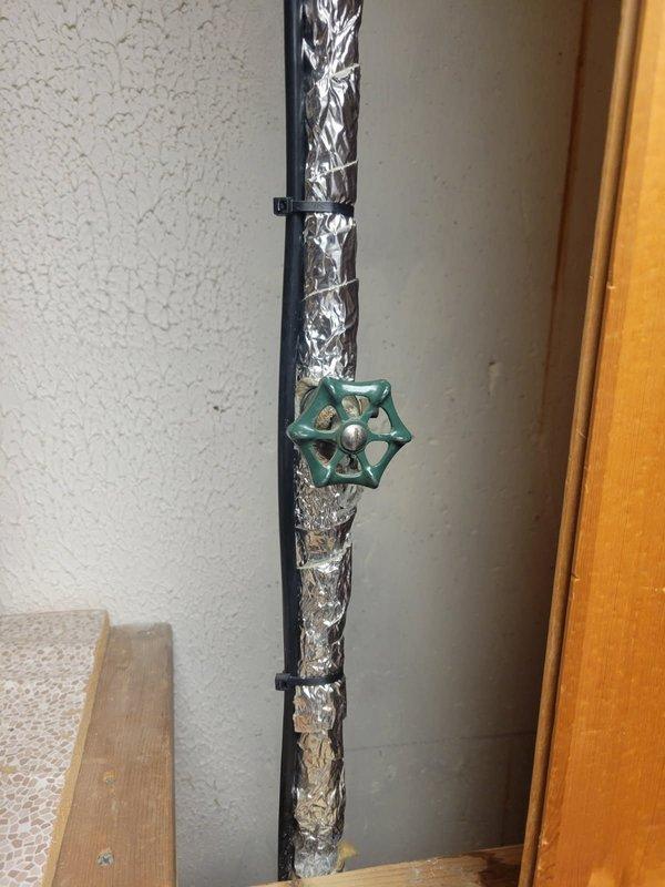 Inspected plumbing system with focus on faucet-related piping. Documented insulated water supply line with green star-shaped shut-off valve secured to wall with mounting brackets. Also examined exposed framing area showing insulated pipe with warning tag running through wooden wall studs adjacent to concrete wall.