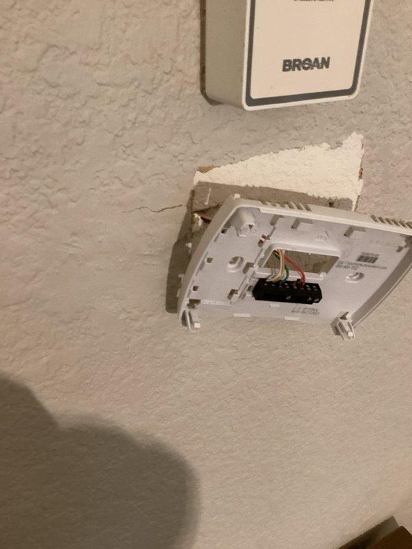 Replaced damaged thermostat that was partially detached from wall mounting plate. Reconnected existing wiring to new unit and repaired damaged drywall section around thermostat installation area where textured wall material had broken away.