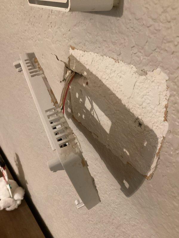 Replaced damaged thermostat that was partially detached from wall mounting plate. Reconnected existing wiring to new unit and repaired damaged drywall section around thermostat installation area where textured wall material had broken away.