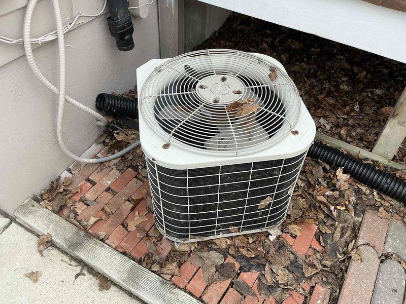 Conducted assessment of existing AC condenser unit installed on brick base platform. Documented debris accumulation around unit and on fan grill. Measured brick paver displacement to evaluate foundation stability for new unit installation.