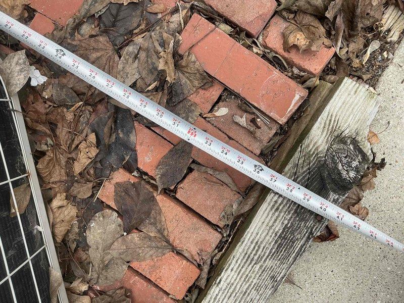 Conducted assessment of existing AC condenser unit installed on brick base platform. Documented debris accumulation around unit and on fan grill. Measured brick paver displacement to evaluate foundation stability for new unit installation.