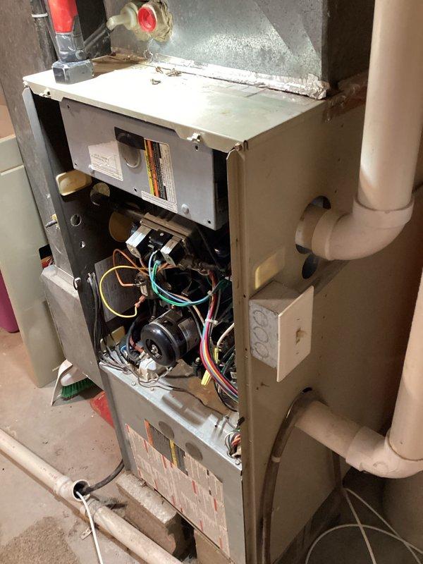 Performed diagnostic inspection on aging furnace unit, accessing internal components by removing front panel. Examined blower assembly, electrical connections, and drainage system. Observed dust accumulation on components and noted normal wear consistent with unit's age, but all systems appear to be in functional working order.