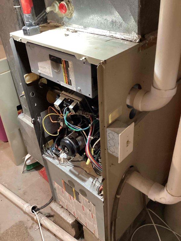 Performed diagnostic inspection on aging furnace unit, accessing internal components by removing front panel. Examined blower assembly, electrical connections, and drainage system. Observed dust accumulation on components and noted normal wear consistent with unit's age, but all systems appear to be in functional working order.