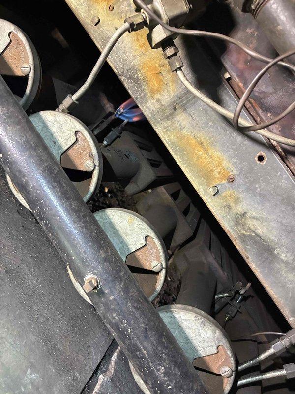 Performed diagnostic inspection of aging boiler system, noting significant corrosion on heat exchanger plate and metal components. Observed burner operation with proper blue flame pattern indicating acceptable combustion efficiency despite equipment age. Documented extensive oxidation on metal surfaces that will require monitoring during future maintenance visits.