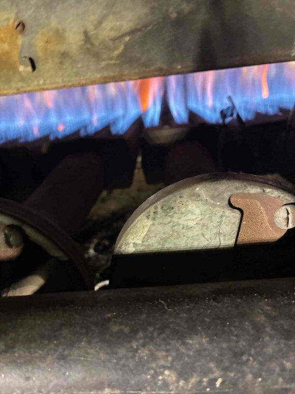 Performed diagnostic inspection of aging boiler system, noting significant corrosion on heat exchanger plate and metal components. Observed burner operation with proper blue flame pattern indicating acceptable combustion efficiency despite equipment age. Documented extensive oxidation on metal surfaces that will require monitoring during future maintenance visits.