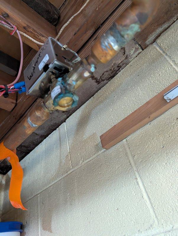 Performed zone valve inspection of hydronic heating system, identifying significant copper pipe corrosion at multiple connection points. Documented control valve with "bedrooms" zone designation and associated wiring (red, pink, blue, black) for control circuit. Noted extensive mineral buildup and oxidation at pipe joints, potentially indicating previous water leakage or ongoing moisture issues requiring future remediation.