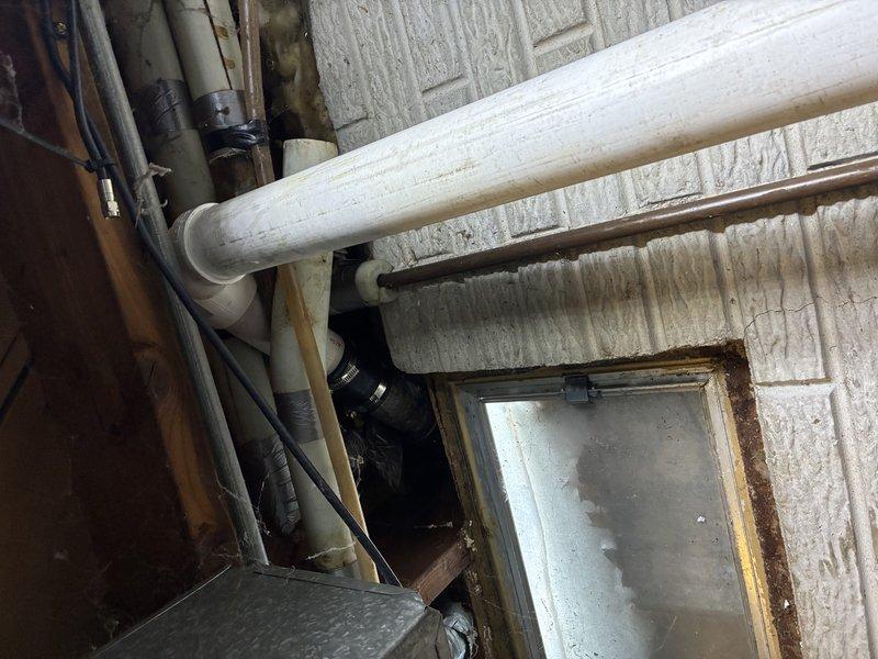 Inspected utility area plumbing infrastructure exhibiting signs of corrosion at metal joints and access panel. Identified and cleared clog in main drainage PVC line, and documented aging copper piping connections that may require future maintenance. Verified proper water flow after service completion.