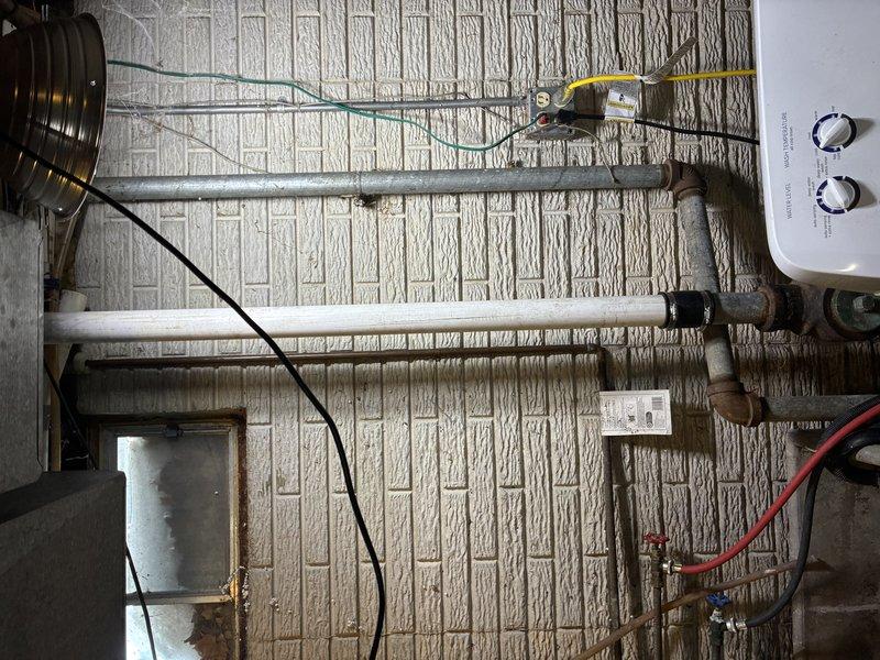 Inspected utility area plumbing infrastructure exhibiting signs of corrosion at metal joints and access panel. Identified and cleared clog in main drainage PVC line, and documented aging copper piping connections that may require future maintenance. Verified proper water flow after service completion.