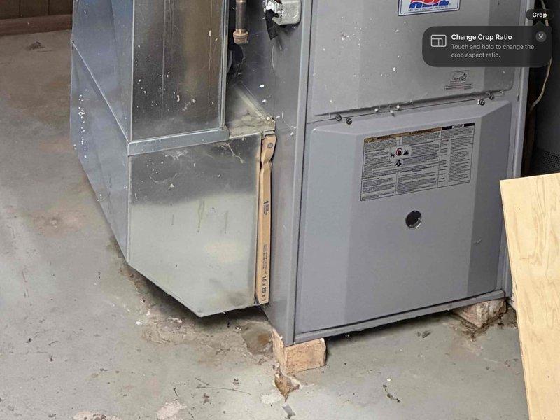 Performed inspection of existing furnace unit showing signs of wear and deterioration. Unit is currently installed on wooden shims over concrete flooring in utility area. Exterior evaluation revealed PVC exhaust pipes requiring proper sealing and alignment with building envelope. Recommended full system replacement due to age and condition of equipment.