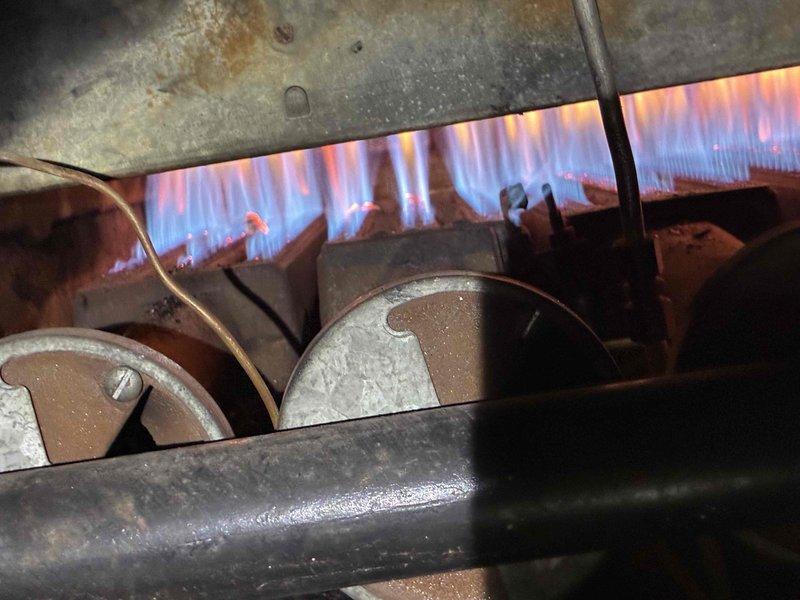 Responded to commercial no-heat call and inspected gas furnace system. Found normal combustion pattern with blue-orange flames visible in heat exchanger with some aging/corrosion but still operational. Checked older Honeywell control device (50-150 range gauge) which exhibited wear but functioning properly; system restored to normal heating operation.