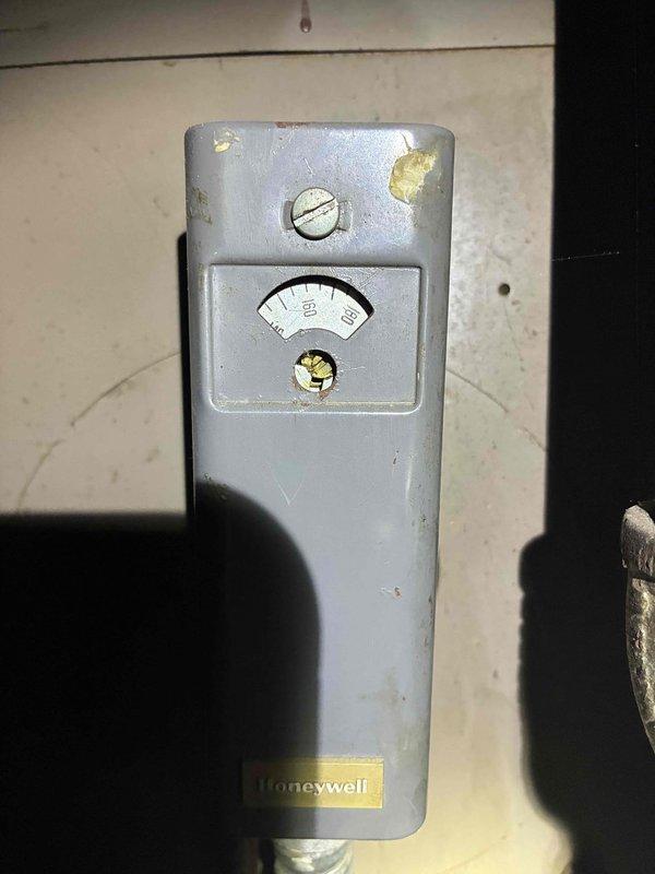 Responded to commercial no-heat call and inspected gas furnace system. Found normal combustion pattern with blue-orange flames visible in heat exchanger with some aging/corrosion but still operational. Checked older Honeywell control device (50-150 range gauge) which exhibited wear but functioning properly; system restored to normal heating operation.