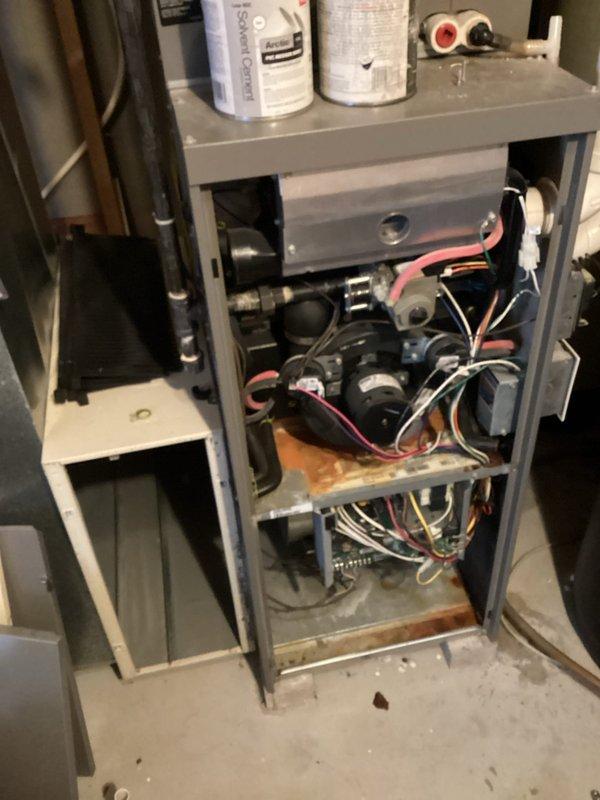 Performed diagnostic inspection on aging furnace system, revealing multiple signs of corrosion and oxidation on the base panel. Examined electrical connections and control board, noting bundled wiring (white, green, orange, yellow, red, and blue) appeared intact despite unit age. Documented interior components and mechanical connections for maintenance planning purposes.
