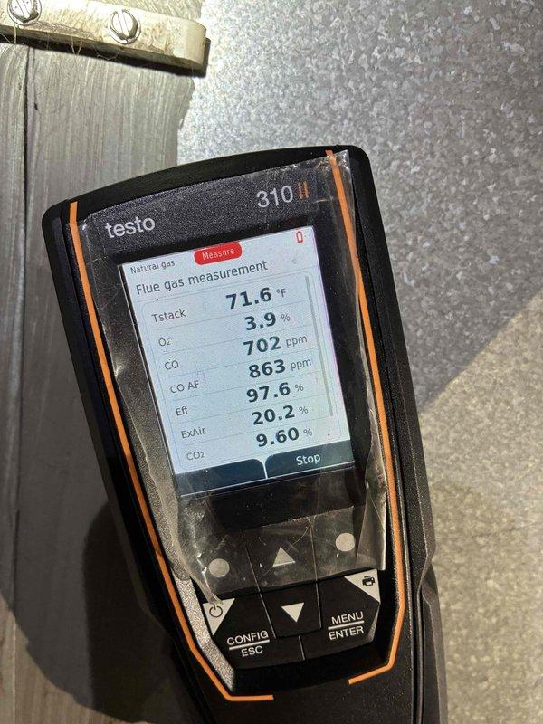 Diagnosed high CO levels (702 ppm/863 ppm AF) during combustion analysis with Testo 310, indicating incomplete combustion despite high efficiency (97.6%). Voltage testing with SC680 multimeter revealed 27.7V at control board, confirming proper voltage to components. Cleaned burner assembly and adjusted gas/air mixture to restore proper combustion parameters and eliminate the no-heat condition.
